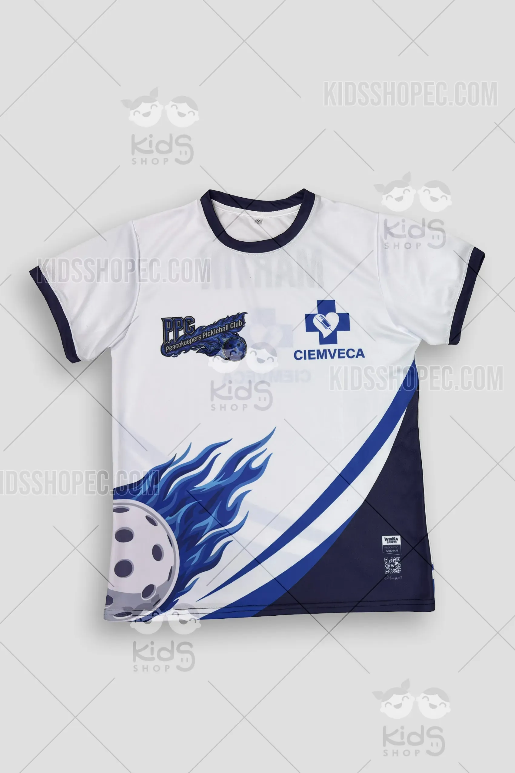 Fotografías del frente y reverso de una camiseta deportiva de manga corta. La prenda es de color blanco con cuello redondo y puños en azul marino. En el pecho presenta los logotipos de "PPC Peacekeepers Pickleball Club" y "CIEMVECA". En la parte inferior izquierda destaca un gráfico vibrante de una pelota de pickleball envuelta en llamas azules, cruzada por franjas diagonales en tonos azul y marino. En la espalda se lee el nombre personalizado "MARTÍN" sobre el logo de CIEMVECA. Lleva la etiqueta original de Winma Sports. Fondo gris neutro con marcas de agua de Kids Shop EC.