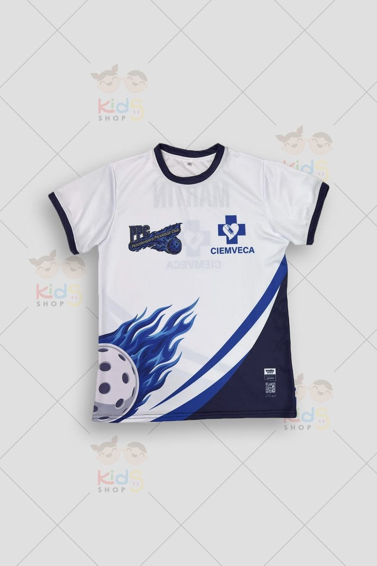 Fotografía de alta resolución de una camiseta deportiva blanca de alto rendimiento. El diseño frontal destaca una pelota de pickleball envuelta en llamas azules y franjas diagonales en tonos azul rey y marino. Incluye logotipos corporativos sublimados de 'CIEMVECA' y 'PPC'. La vista posterior muestra el nombre personalizado 'MARTÍN' en la parte superior. Cuello redondo y puños en color marino oscuro. Etiqueta de autenticidad Winma Sports visible en la zona inferior. Fondo gris claro con marcas de agua de Kids Shop EC.
