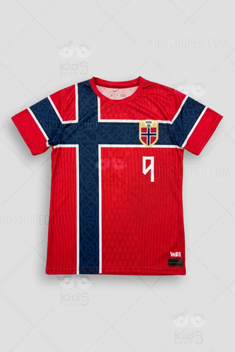 Fotografías de estudio en formato flat lay y primeros planos de una camiseta de fútbol de manga corta en color rojo vibrante con temática de la selección noruega. Presenta un diseño de cruz nórdica en azul oscuro que se extiende por el frente y la espalda, con un sutil patrón de nudos vikingos y runas en su interior. En el pecho derecho destaca un escudo dorado con forma de blasón que contiene la bandera de Noruega y la palabra "NORGE" en mayúsculas, junto a un pequeño número 9 dorado. La espalda muestra el apellido "BRAUT HAALAND" en letras mayúsculas blancas y un gran dorsal número 9 en color blanco con contorno negro. Los puños de las mangas y el dobladillo inferior incluyen franjas horizontales.