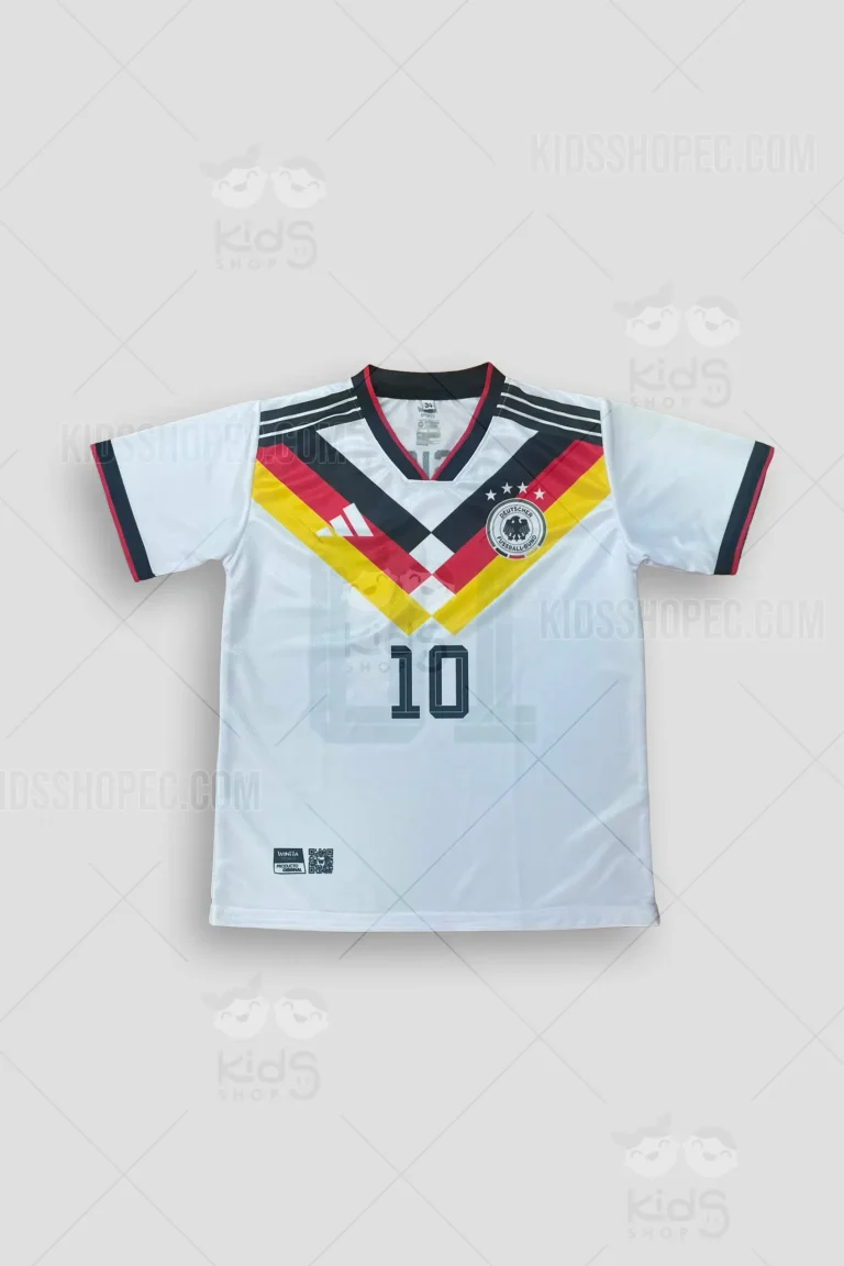 Fotografías de estudio de una camiseta de fútbol de manga corta, color blanco con un diseño en el pecho en forma de "V" con gruesas franjas en negro, rojo y amarillo. Presenta cuello en 'V' y puños con finos ribetes tricolores. En el pecho izquierdo lleva estampado un escudo circular con un águila negra y cuatro estrellas, además de un logotipo deportivo y el número 10 oscuro en el centro. En la espalda destaca el nombre 'MUSIALA' sobre un gran número 10 con un diseño de líneas que simula efecto de sombra. Vistas frontales, traseras y detalles de primer plano sobre un fondo gris claro.