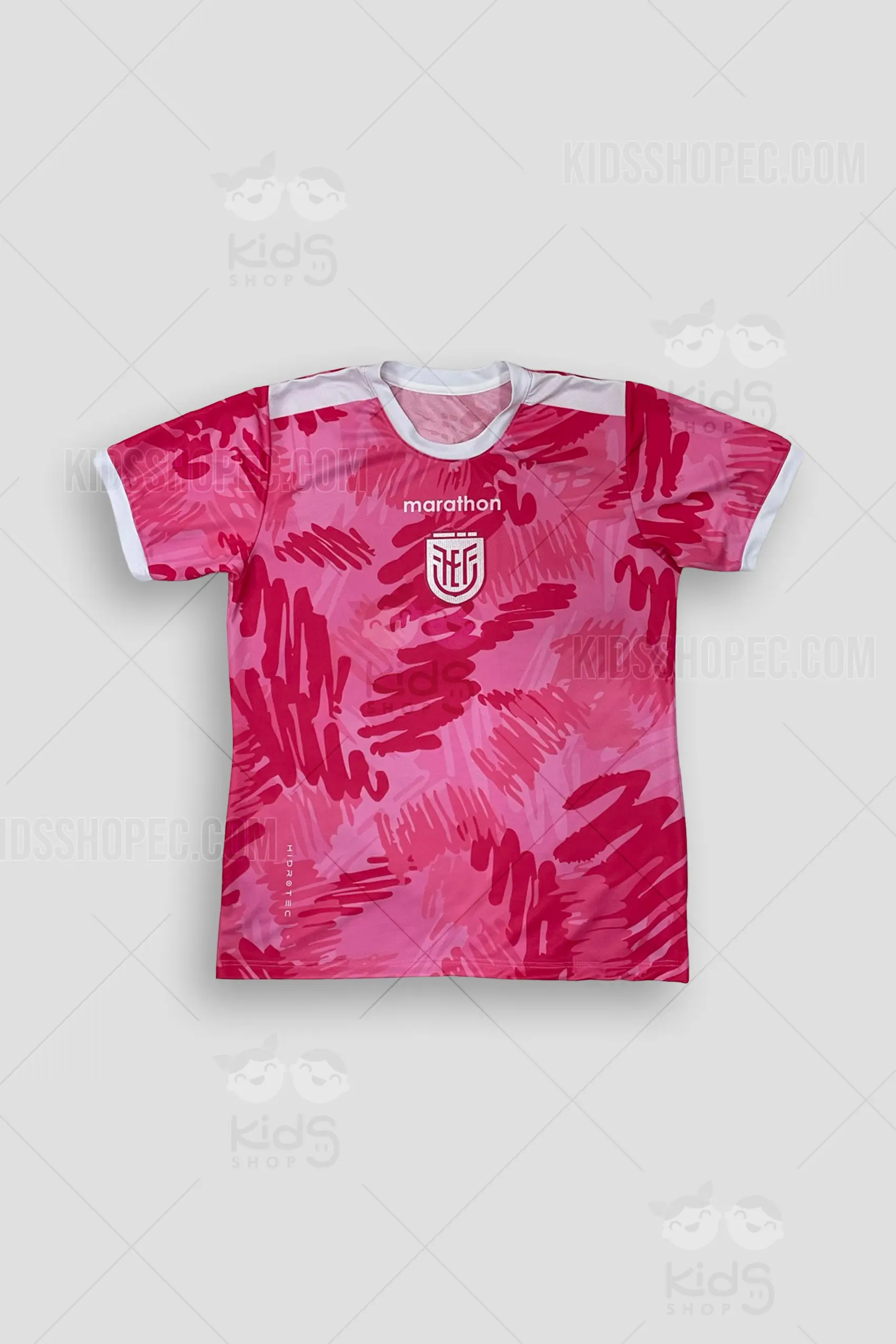 Fotografías de estudio de una camiseta deportiva de manga corta destacada por su vibrante color rosado y un patrón abstracto de trazos dinámicos en tonos magenta y rosa claro. Presenta cuello redondo y bordes de las mangas en color blanco contrastante. En el centro del pecho lleva estampado en color blanco un escudo deportivo representativo del fútbol ecuatoriano junto a letras de estilo deportivo. Las imágenes muestran la vista frontal completa, un primer plano de los detalles del pecho y la espalda limpia sobre un fondo gris claro.