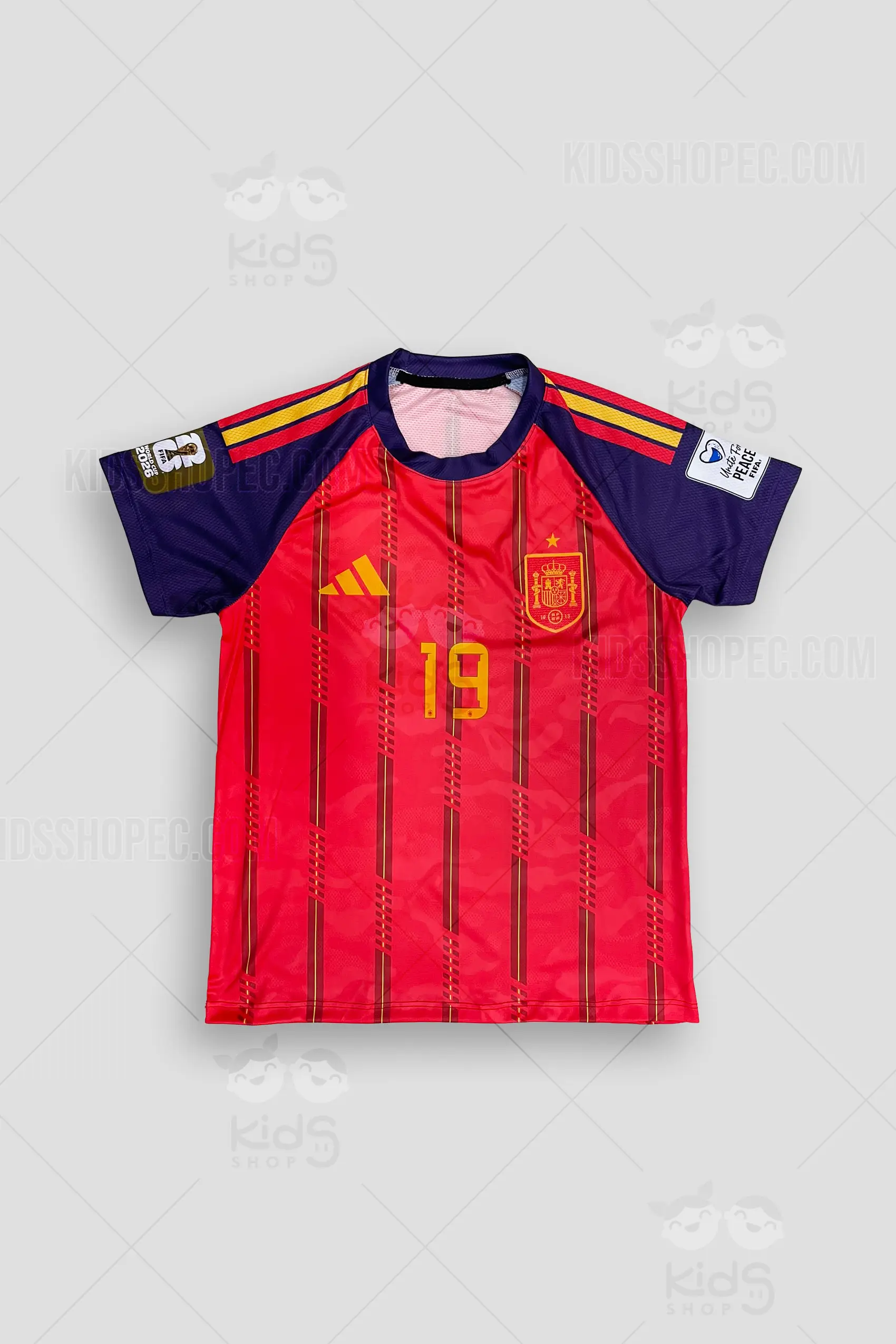 Fotografías de estudio de una camiseta de fútbol manga corta, base color rojo vibrante con un patrón de líneas verticales oscuras y acentos amarillos. Las mangas contrastan en color azul profundo con detalles de rayas en los hombros y parches en las mangas. En el pecho izquierdo lleva un escudo rojo y dorado con una corona y una estrella, acompañado del número 19 en dorado en el centro. En la espalda destaca el texto del jugador sobre un número 19 grande en color dorado. Vistas detalladas del estampado frontal, dorsal y plano general sobre un fondo gris claro.