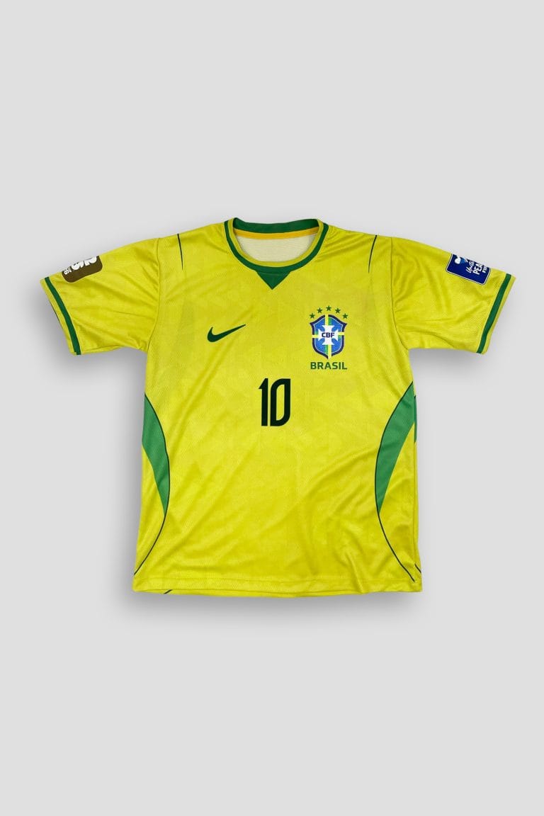 Fotografías de estudio de una camiseta de fútbol de manga corta, color amarillo vibrante con detalles anatómicos en color verde en el cuello y los costados. En la parte frontal lleva estampado el número 10, un detalle similar a un visto deportivo y un escudo azul con estrellas y la palabra 'BRASIL'. En la espalda destaca el nombre 'NEYMAR JR.' impreso sobre un número 10 grande en color verde oscuro. Las imágenes muestran vistas detalladas del frente y reverso sobre un fondo gris claro.