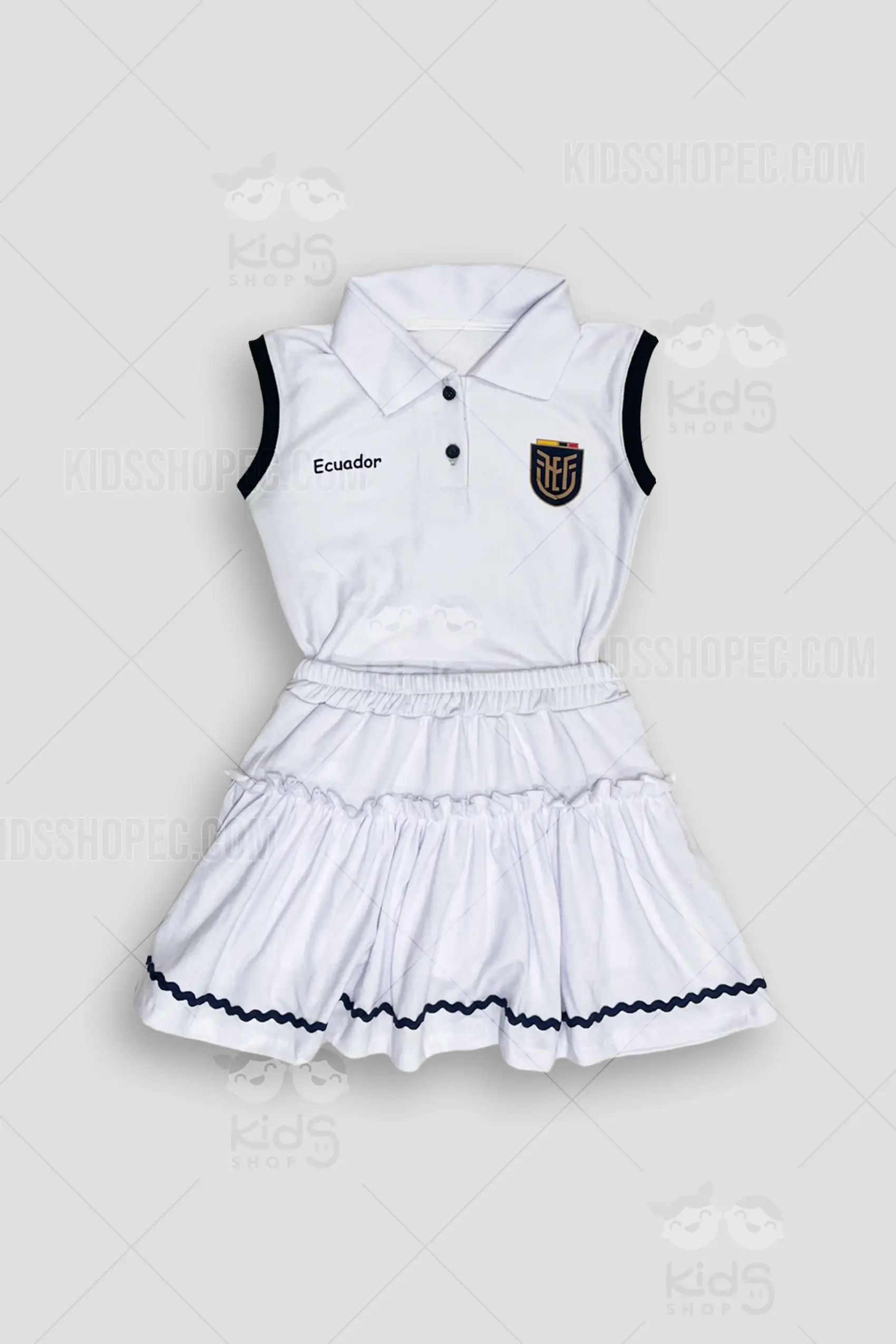 Fotografías de estudio de un conjunto deportivo infantil de dos piezas para niña en color blanco. Incluye una blusa tipo polo sin mangas con bordes azul marino, botones oscuros, la palabra 'Ecuador' y un escudo deportivo tricolor en el pecho. En la espalda lleva estampado el contorno del mapa del país y la frase 'La piel que nos une' en color oscuro. Se complementa con una falda blanca de volantes escalonados, cintura elástica y un detalle ondulado azul marino en el borde inferior. Fondo gris claro.