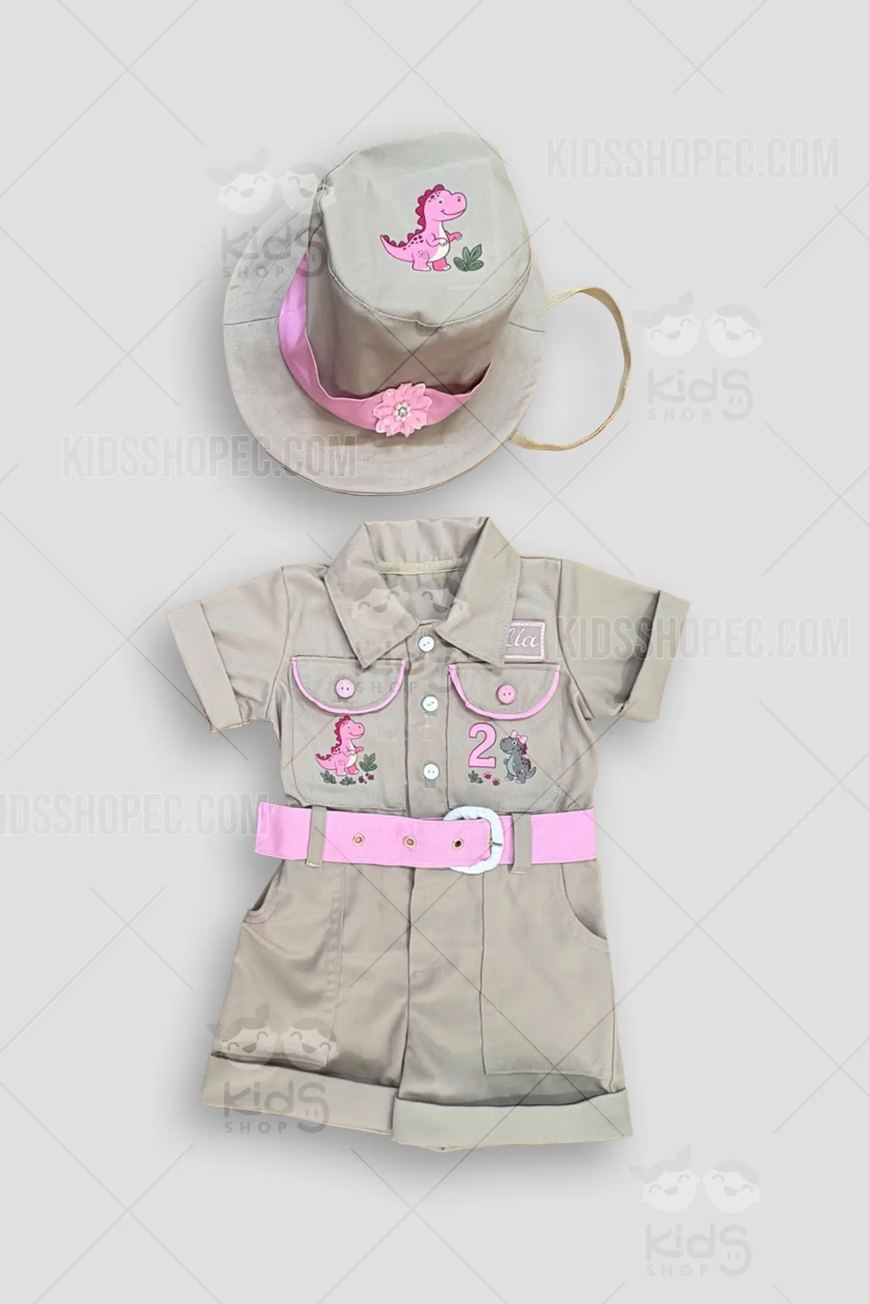 Fotografías de estudio en formato flat lay de un conjunto infantil de explorador o safari en color beige con detalles en rosa. El traje tipo enterizo de manga y pantalón corto presenta un cuello camisero, cinturón rosa con hebilla blanca, y ribetes rosas en las solapas de los bolsillos del pecho. Incluye estampados de adorables dinosaurios rosas y grises, el número 2 y un parche con el nombre "Sofía". Se acompaña de un sombrero de explorador beige a juego, decorado con una cinta rosa, un aplique de flor y el estampado de un pequeño dinosaurio.