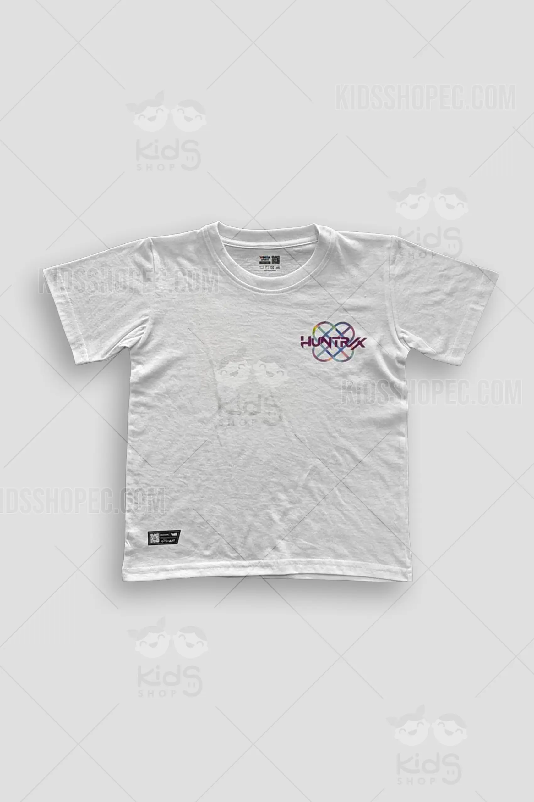 Fotografías de estudio en formato flat lay de una camiseta de manga corta en color blanco sólido con cuello redondo. La parte frontal muestra un logotipo en el pecho izquierdo con el texto "HUNTRX" sobre un símbolo geométrico entrelazado multicolor, acompañado de una etiqueta negra decorativa en el dobladillo inferior izquierdo. La parte posterior presenta un gran estampado principal que ilustra a tres chicas estilo K-pop animado y una mascota de gato azul, enmarcados dentro de una gran estrella morada con detalles de semitonos, coronado por la palabra "HUNTRX" en tipografía estilizada.
