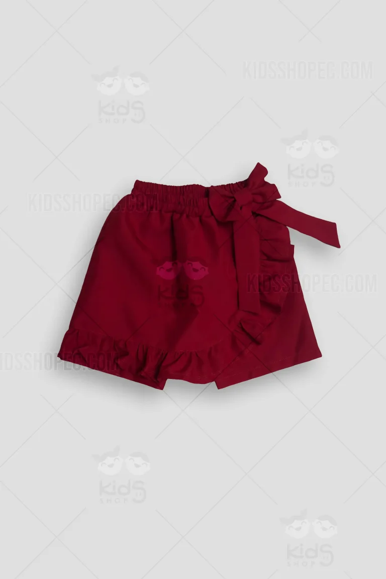 Fotografías de estudio en formato flat lay de una falda short infantil en color rojo vino sólido. La prenda presenta una cintura elástica fruncida y un diseño cruzado en la parte frontal. Está decorada con vuelos ondulados a lo largo del borde inferior y en la apertura frontal, y se complementa con un lazo cosido en la cintura. La parte posterior muestra el diseño liso del short base.
