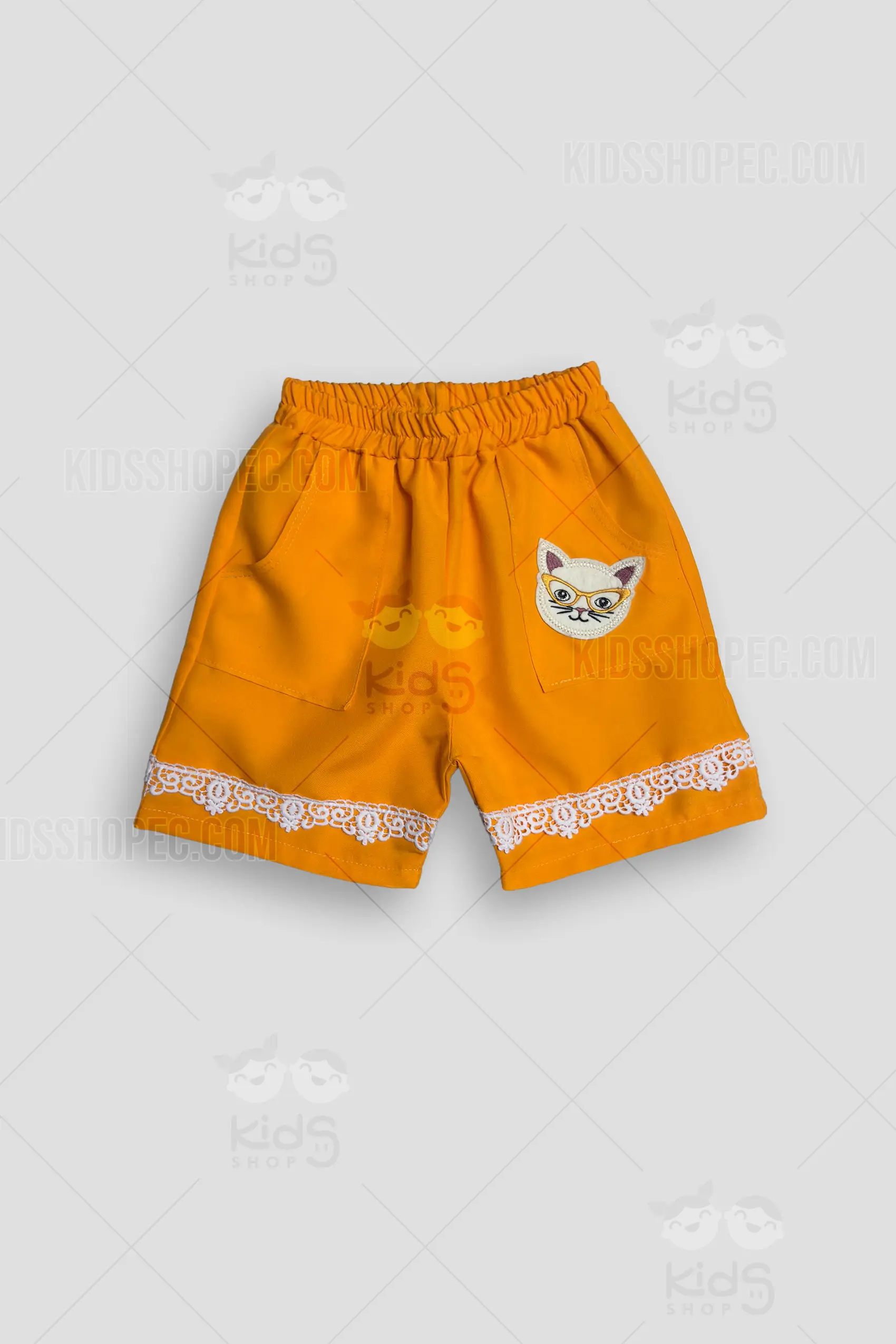 Fotografías de estudio en formato flat lay de un pantalón corto (short) infantil en color naranja vibrante. La prenda cuenta con cintura elástica fruncida y dos amplios bolsillos frontales. En la zona del bolsillo izquierdo destaca un aplique decorativo con el rostro de un gato blanco usando lentes amarillos. Los dobladillos inferiores de ambas piernas están adornados con una delicada cinta de encaje blanco con patrones florales. La parte posterior muestra la tela lisa resaltando el detalle del encaje en el borde.