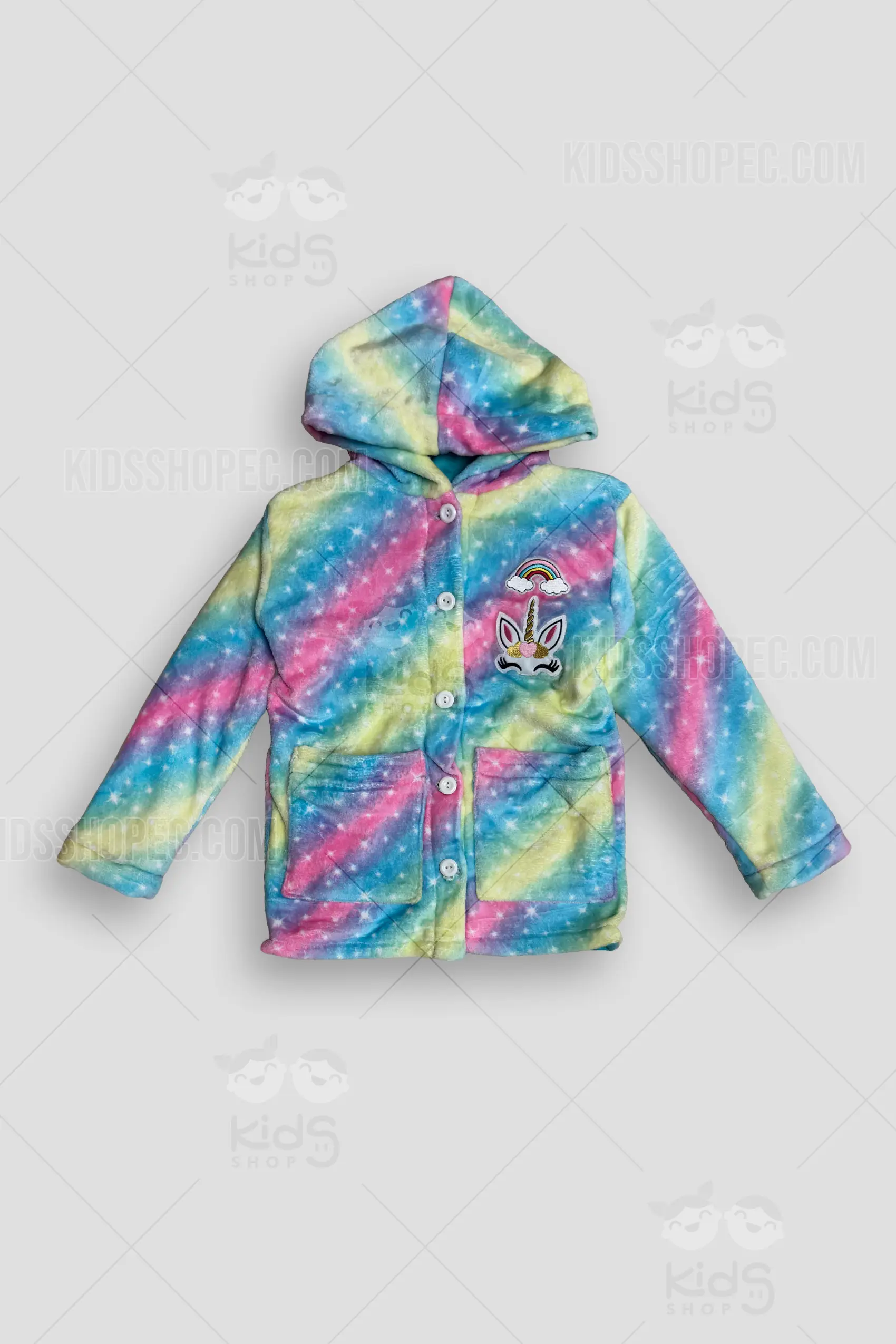 Fotografías de estudio en formato flat lay de una chaqueta infantil con capucha, confeccionada en tela de peluche suave. Presenta un patrón colorido de franjas diagonales estilo galaxia arcoíris en tonos rosa, azul y amarillo, salpicado de estrellas blancas. La prenda cuenta con cierre frontal de botones blancos, dos bolsillos cuadrados en la parte inferior y detalles decorativos en el pecho izquierdo consistentes en dos apliques: un arcoíris y un rostro de unicornio dorado. La parte posterior muestra la continuidad del patrón arcoíris estrellado.